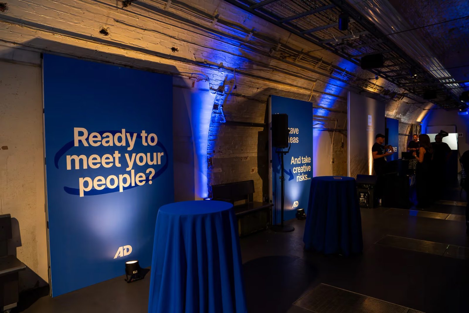 Large blue AdPower foamex panel reading Ready to meet your people beside the uplit brick arches at Mail Rail