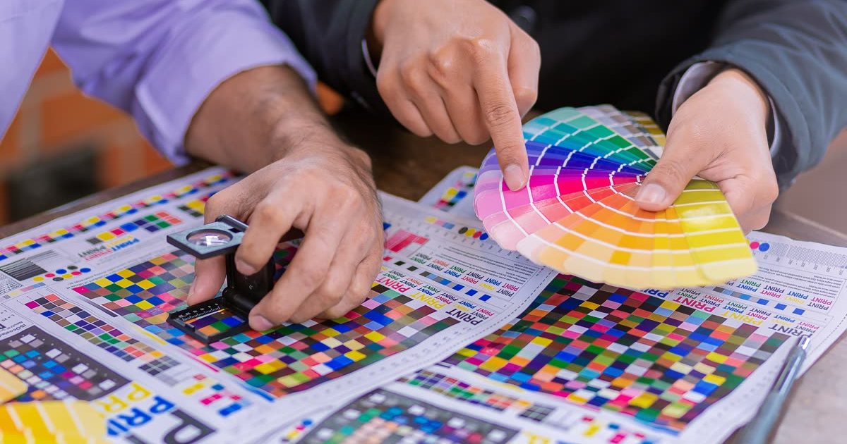 Checking CMYK test prints with a loupe and colour swatches
