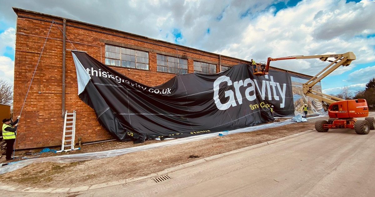 Gravity Smart Campus mesh building wrap being installed on a brick warehouse
