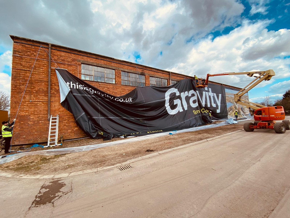 Installers hanging a giant printed banner across a brick building