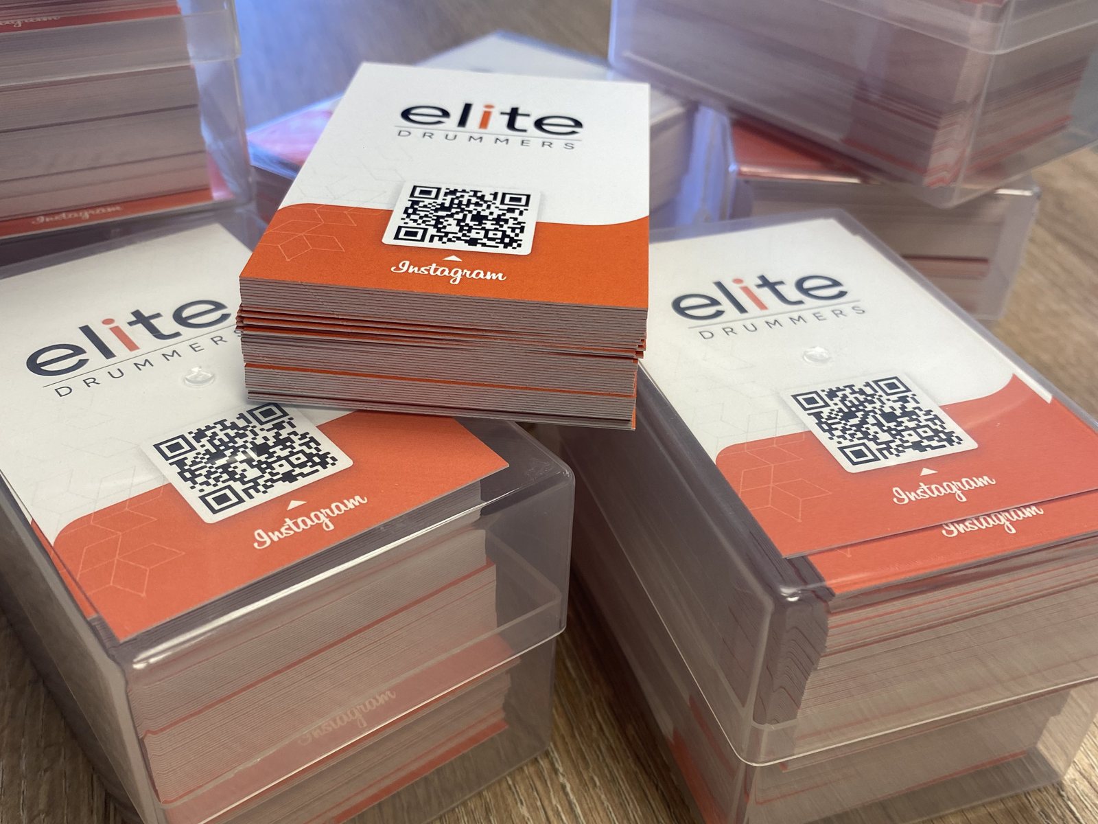 Stacks of Elite Drummers business cards with an orange design and Instagram QR code, printed by Print Station