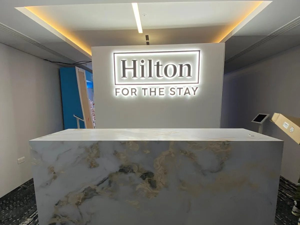 Halo lit Hilton For The Stay logo above a marble effect reception desk