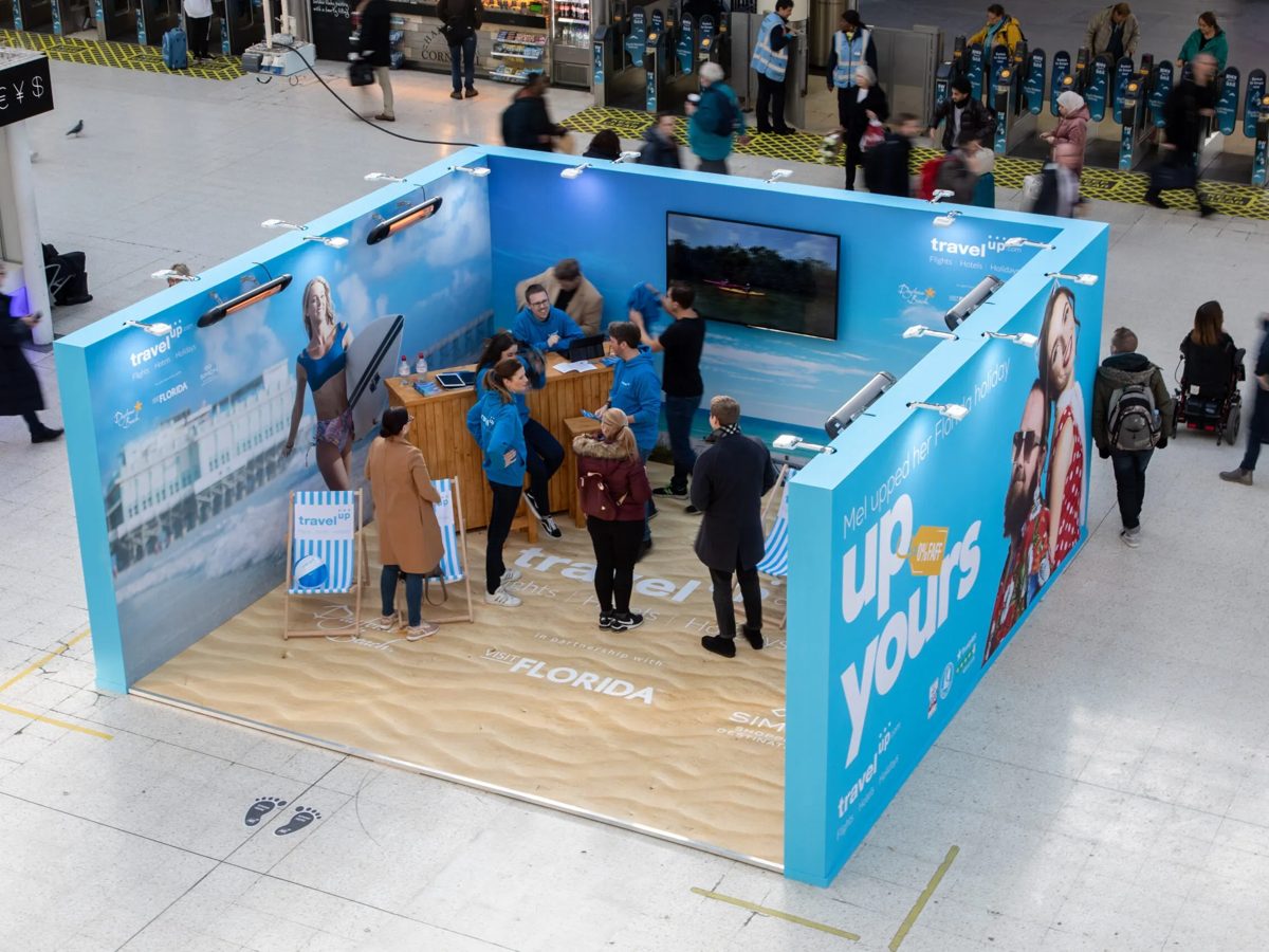 Travelup beach pop up with printed campaign walls and sand effect floor on the Waterloo concourse