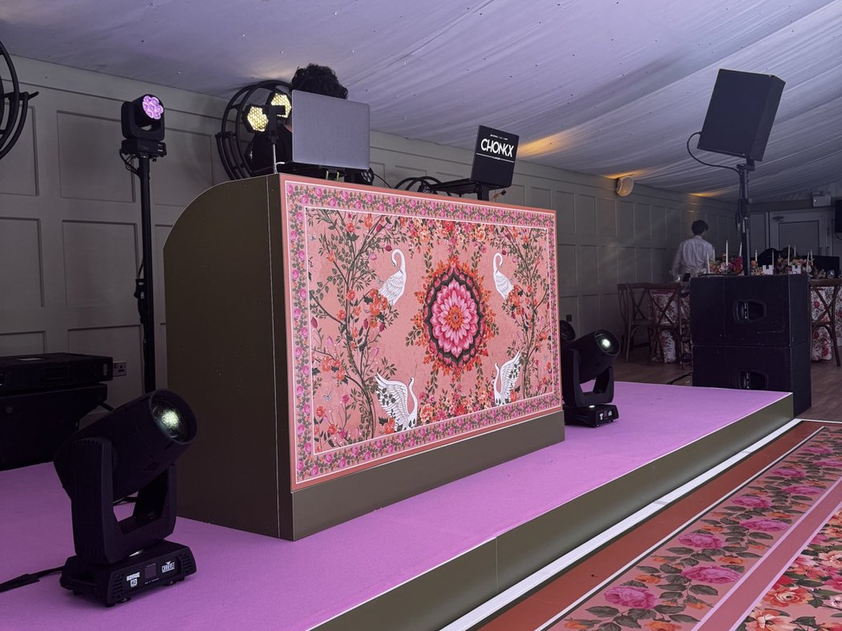 DJ booth wrapped in a printed pink floral and swan design on a marquee stage