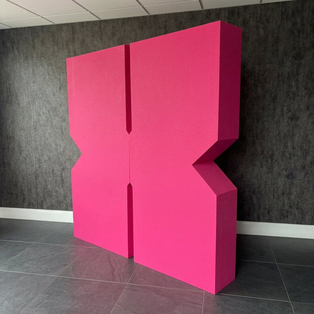 Giant hot pink 3D foam letter X, CNC cut to shape and painted, standing in the Print Station showroom