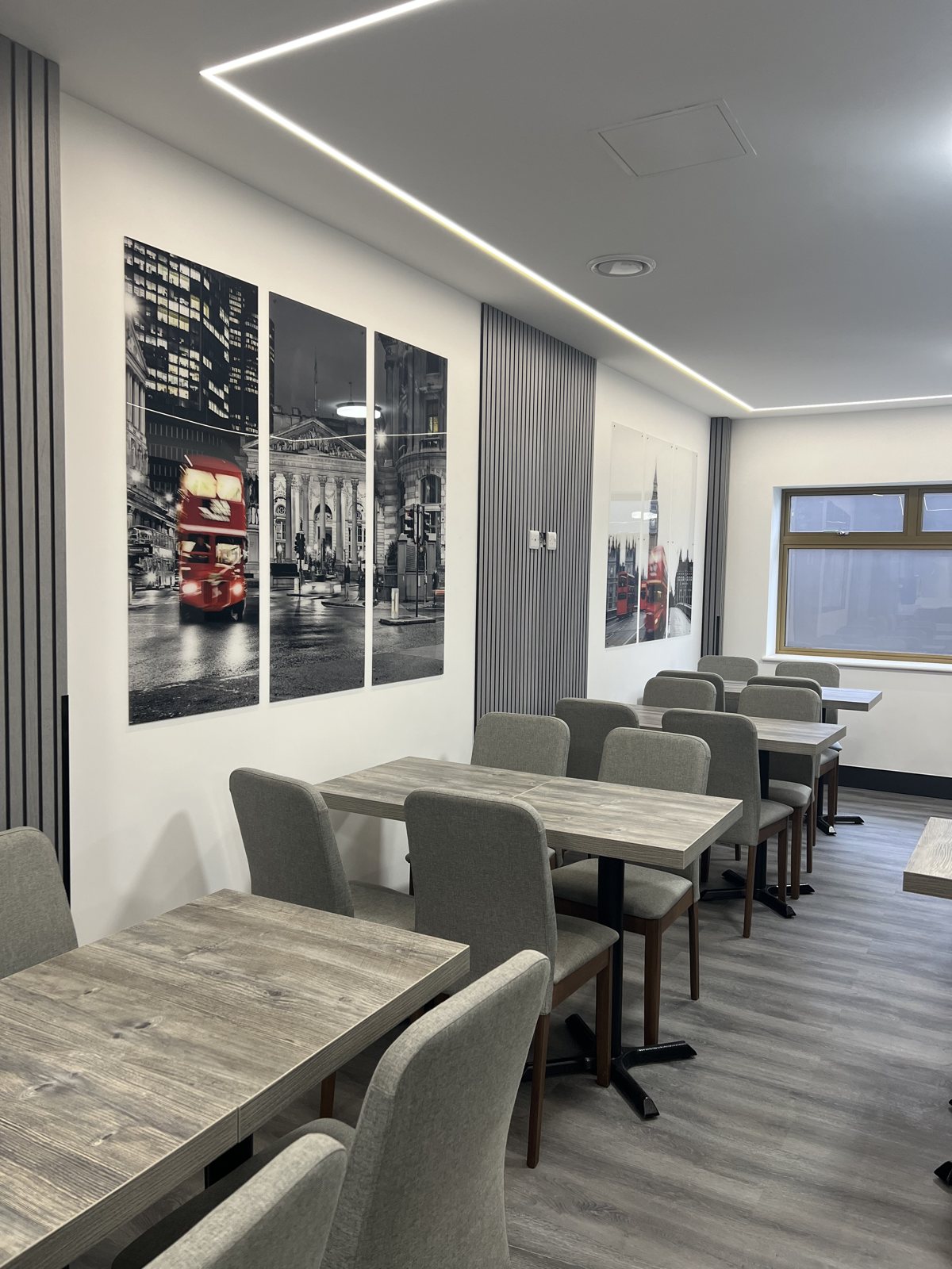 Hotel canteen with reverse printed acrylic triptychs of red London buses at Bank and Westminster on white walls between grey slatted panels