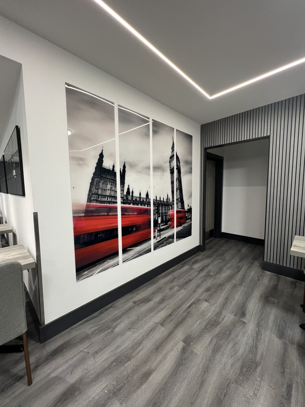 Four panel reverse printed acrylic of a red London bus speeding past the Houses of Parliament and Big Ben, mounted on a hotel canteen wall