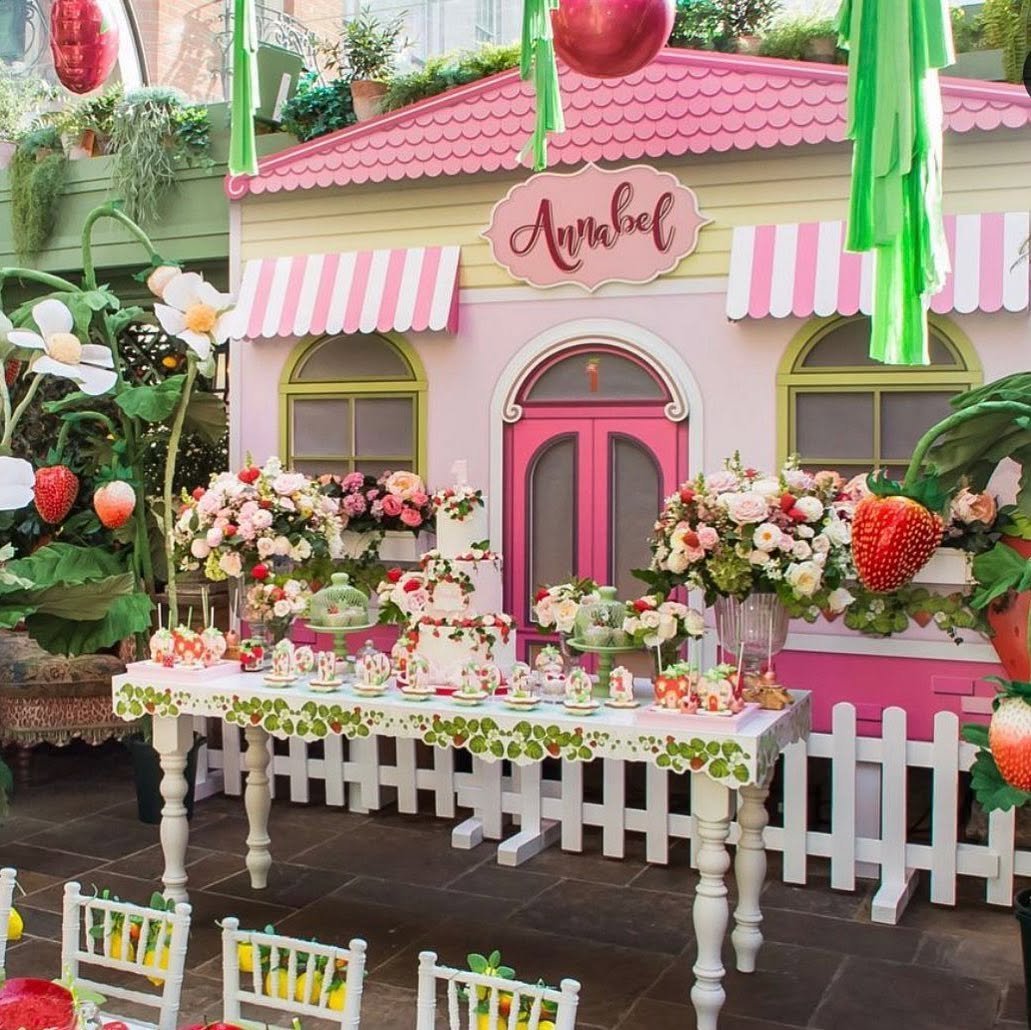 Giant pink and cream dolls house backdrop with an Annabel sign, striped awnings and a picket fence behind a strawberry themed dessert table