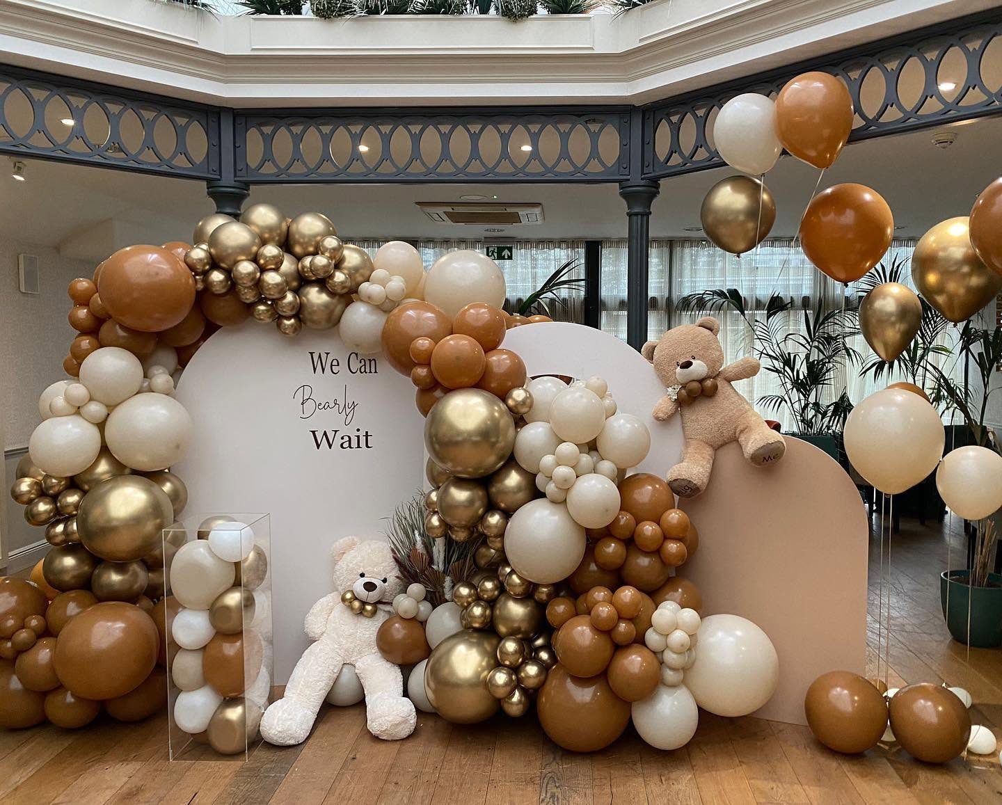 We Can Bearly Wait teddy bear party backdrop with cream and blush arches, gold, caramel and ivory balloons and plush teddies