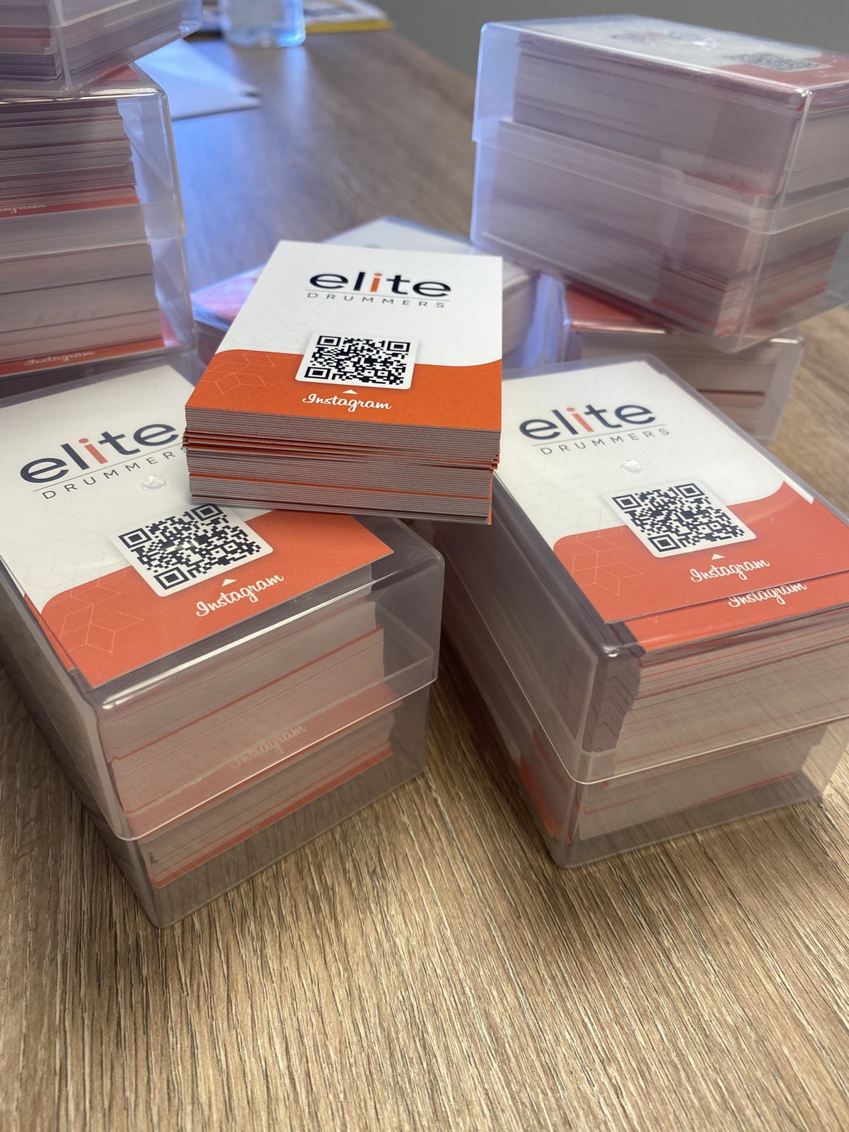 Stacks of Elite Drummers business cards with an orange design and Instagram QR code, boxed and ready to hand out