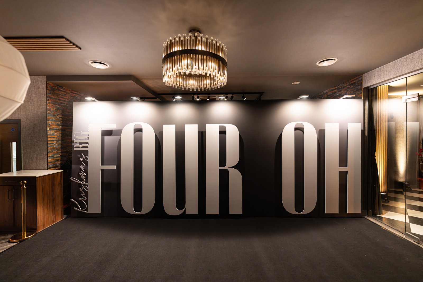 Bespoke black UV Blackback Textile (Canvas) photo op with giant 3D white FOUR OH foamex letters for a fortieth birthday, lit beneath a crystal chandelier