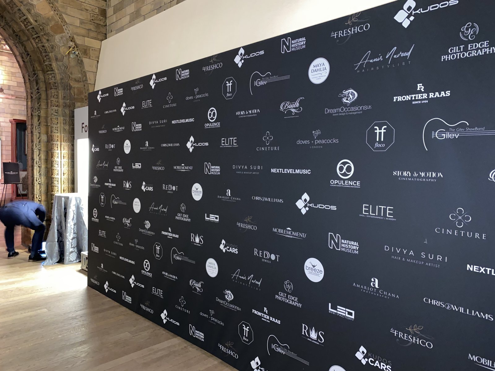 Giant black step and repeat media wall printed on canvas with white sponsor logos, set up inside the Natural History Museum, London