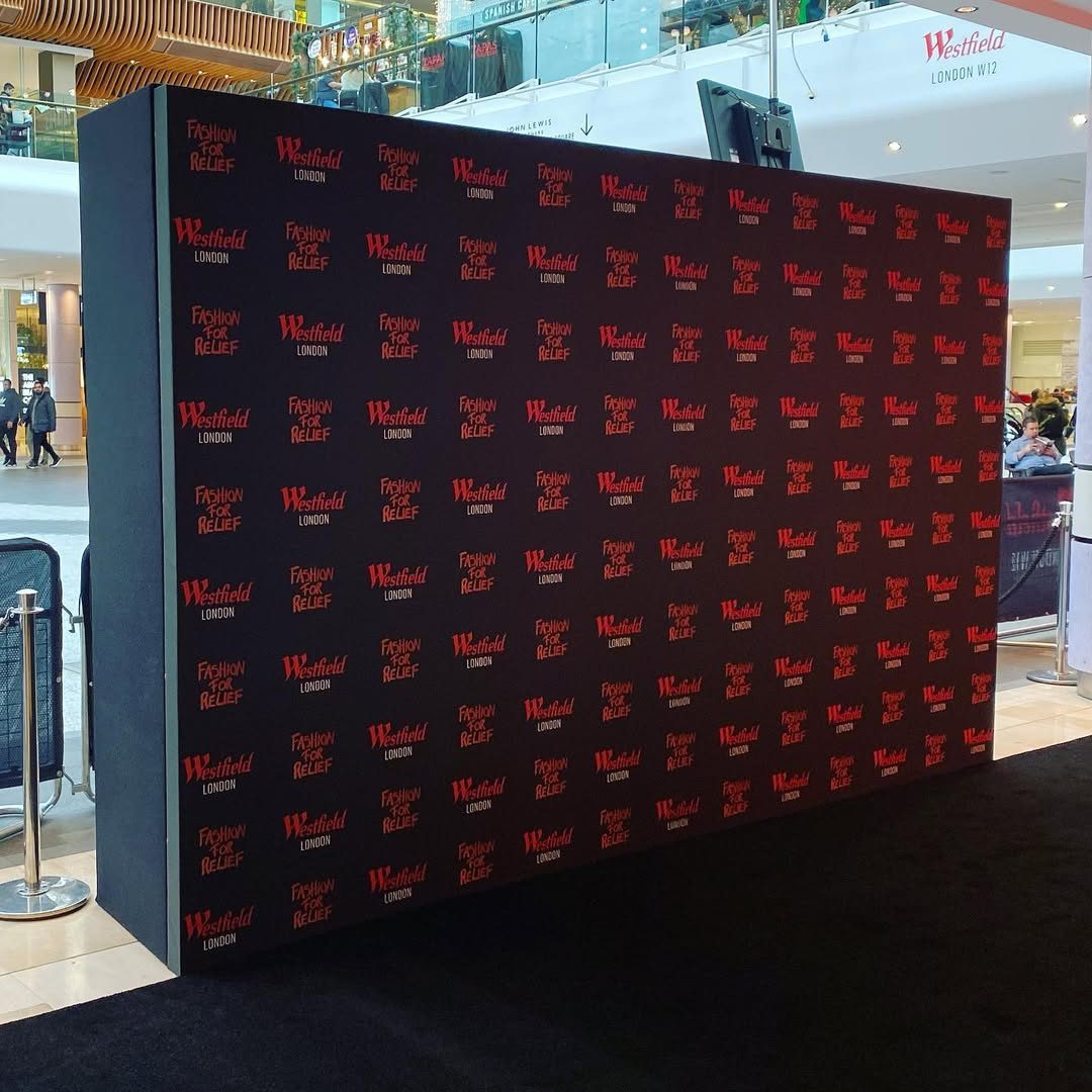 Black step and repeat media wall printed with red Westfield London and Fashion for Relief logos on a black carpet inside Westfield London