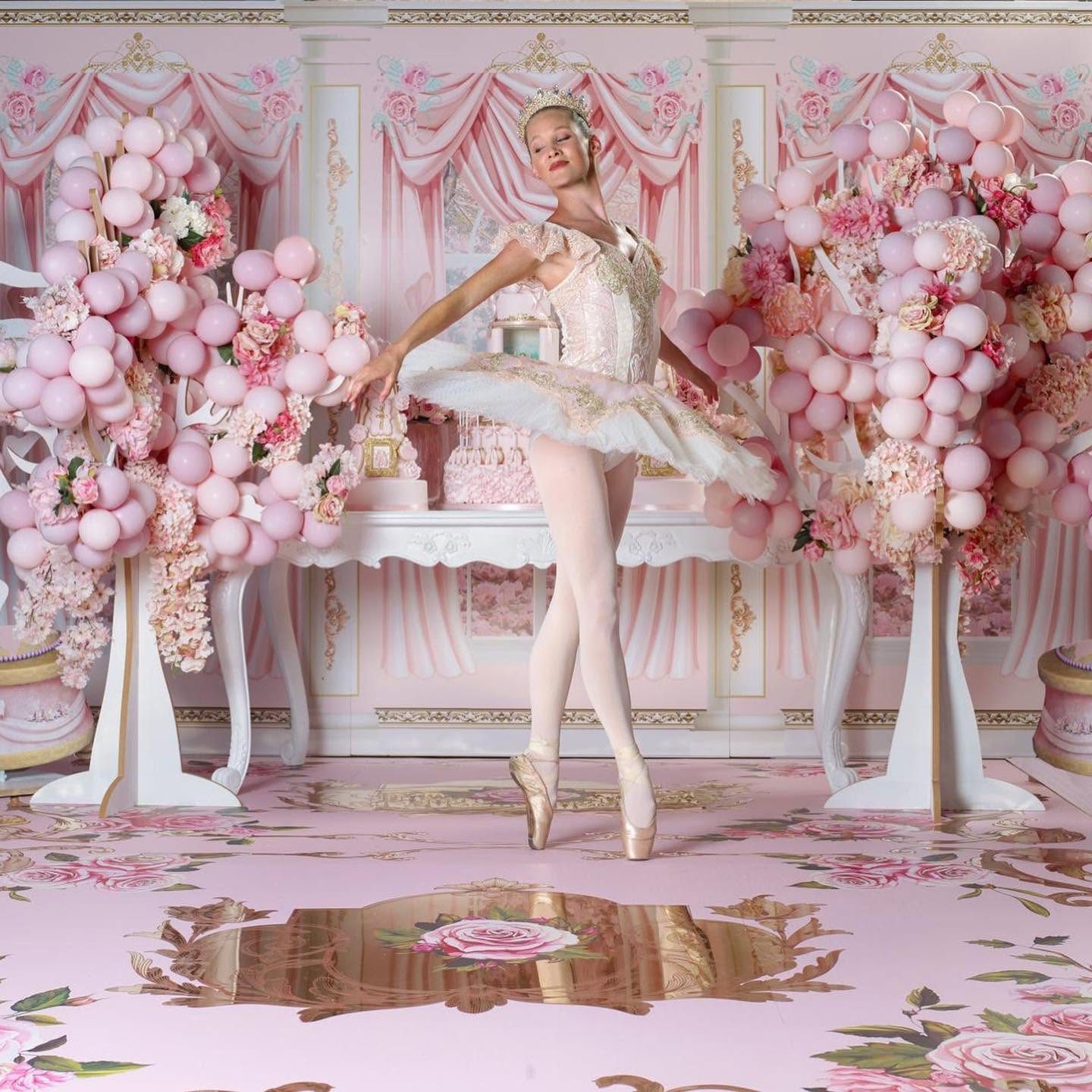 Ballerina on pointe on a bespoke pink dance floor printed with roses and ornate gold mirror scrollwork, framed by pink balloon and flower displays