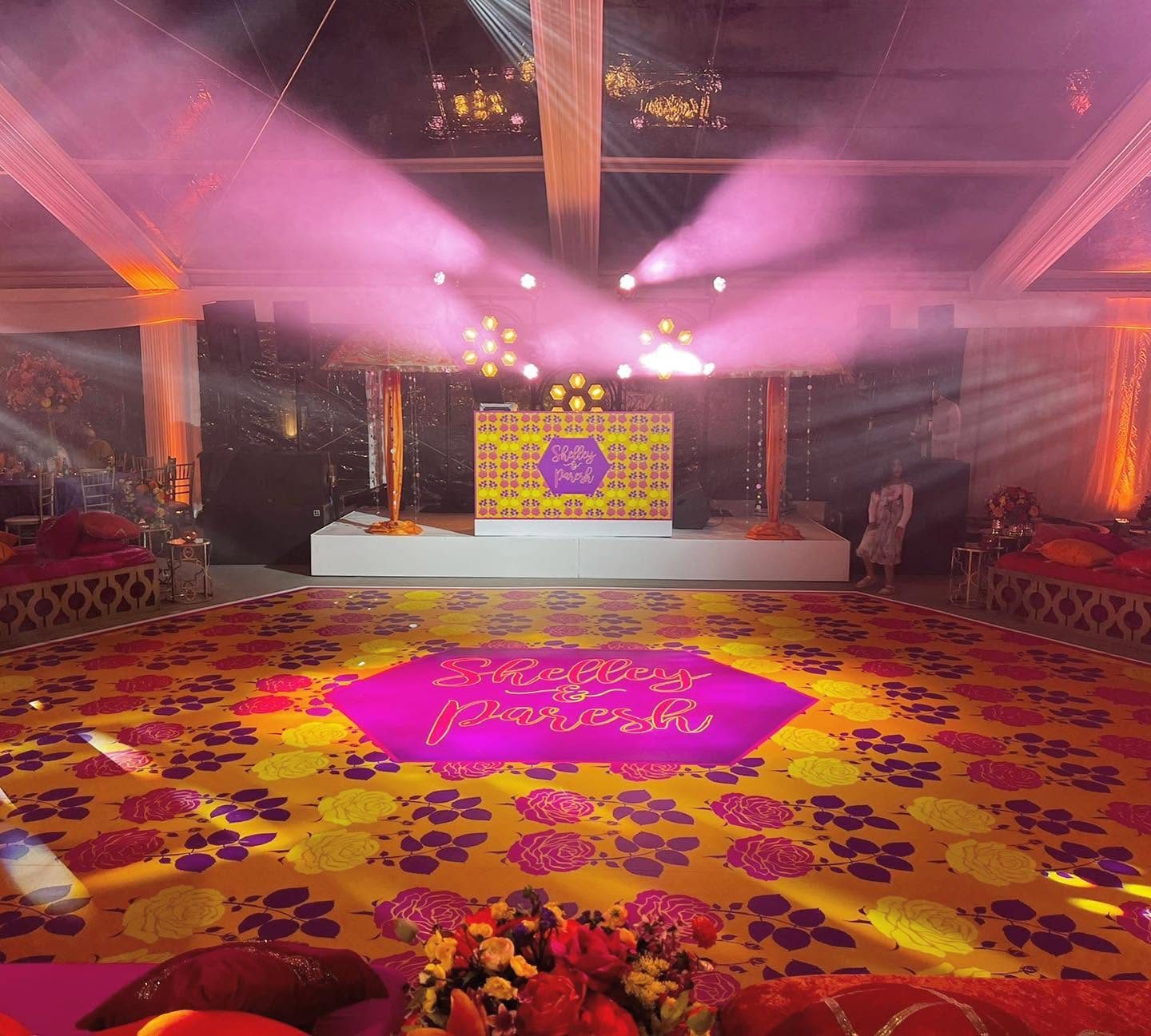 Vibrant mustard dance floor printed with pink and yellow roses and purple leaves, with a hot pink hexagon centrepiece reading Shelley and Paresh