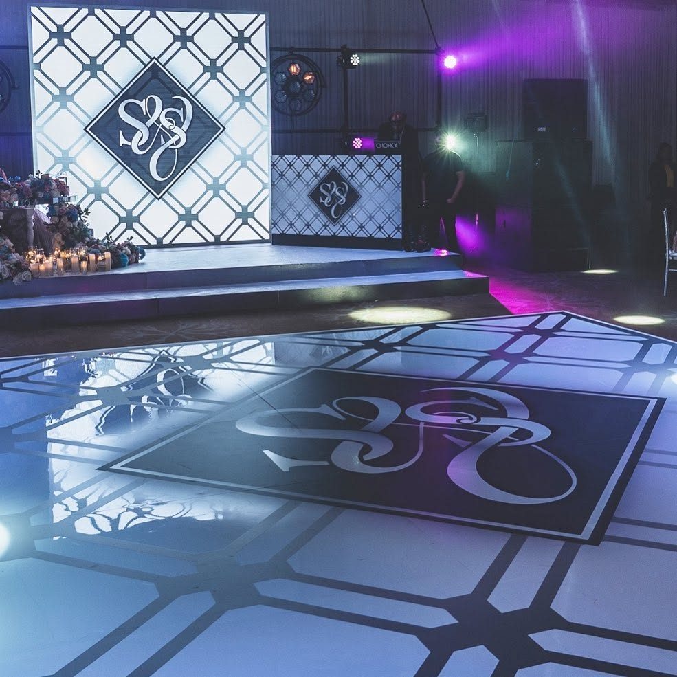 White dance floor printed with a navy lattice pattern and a large diamond monogram, matching the stage backdrop and DJ booth behind it
