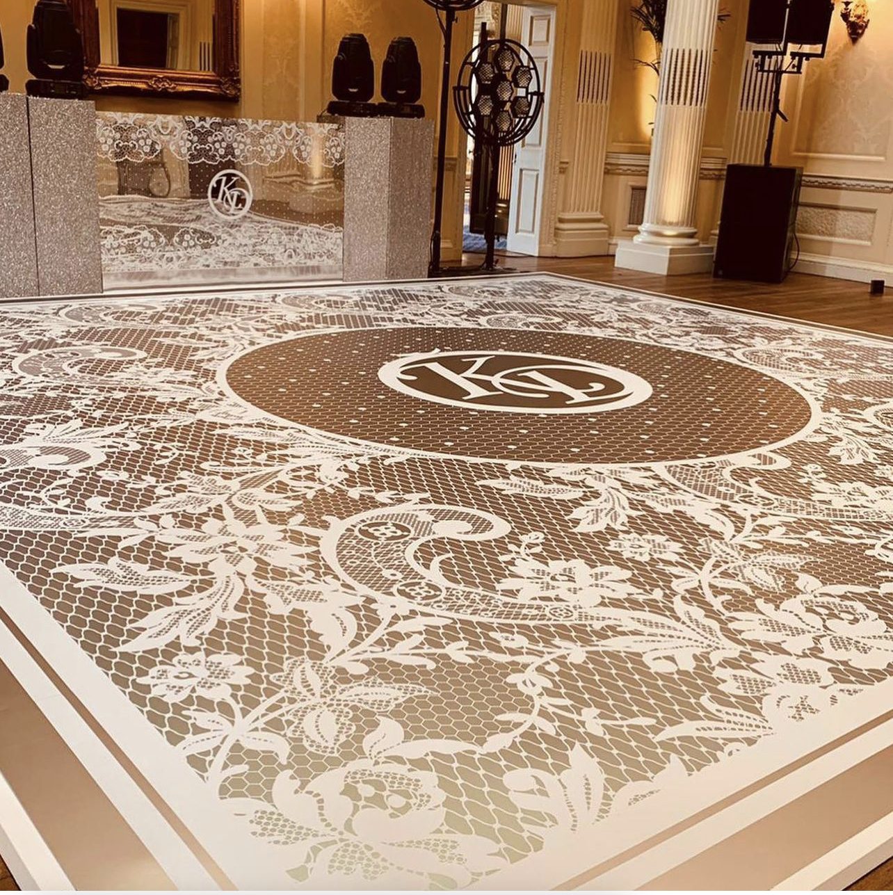 Rose gold printed wedding dance floor with a white lace floral pattern and the couple's monogram in a grand ballroom