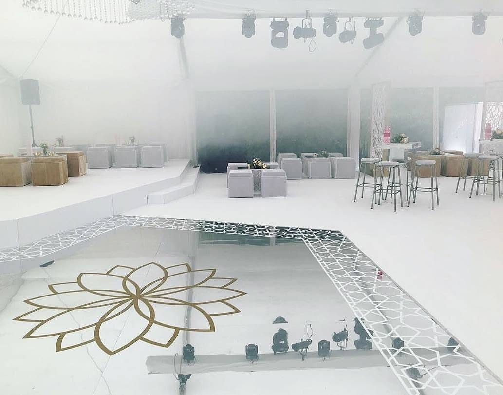 Custom shaped silver mirror dance floor with a gold lotus motif and an intricate white geometric lattice border in an all white marquee