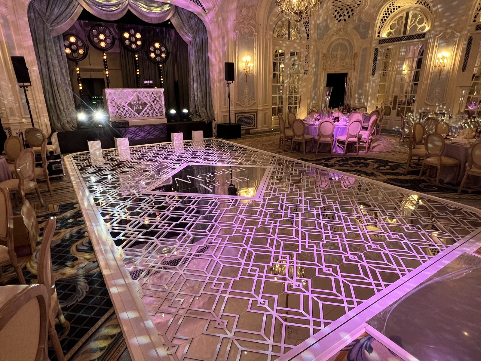Silver mirror dance floor printed with white geometric patterns and a monogram, with a matching DJ booth in an ornate ballroom