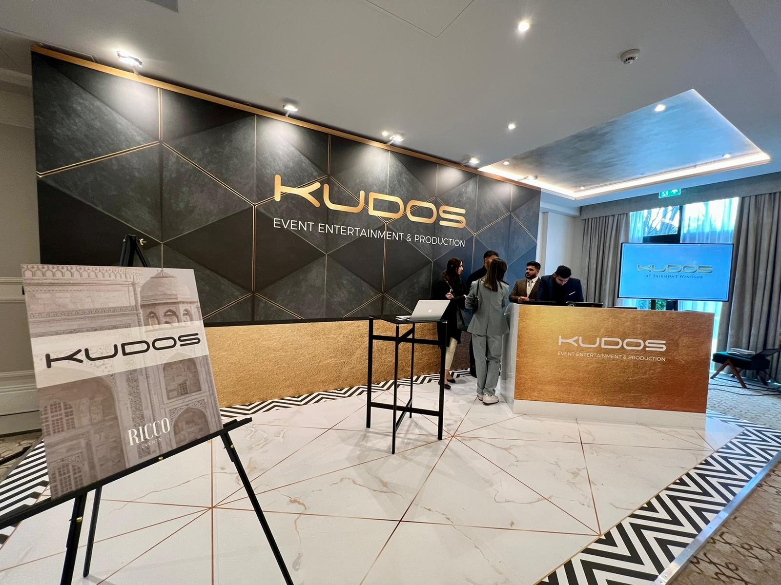 Kudos exhibition stand at Fairmont Windsor with black and gold geometric canvas wrapped walls, printed marble effect flooring with a chevron border and a gold printed counter