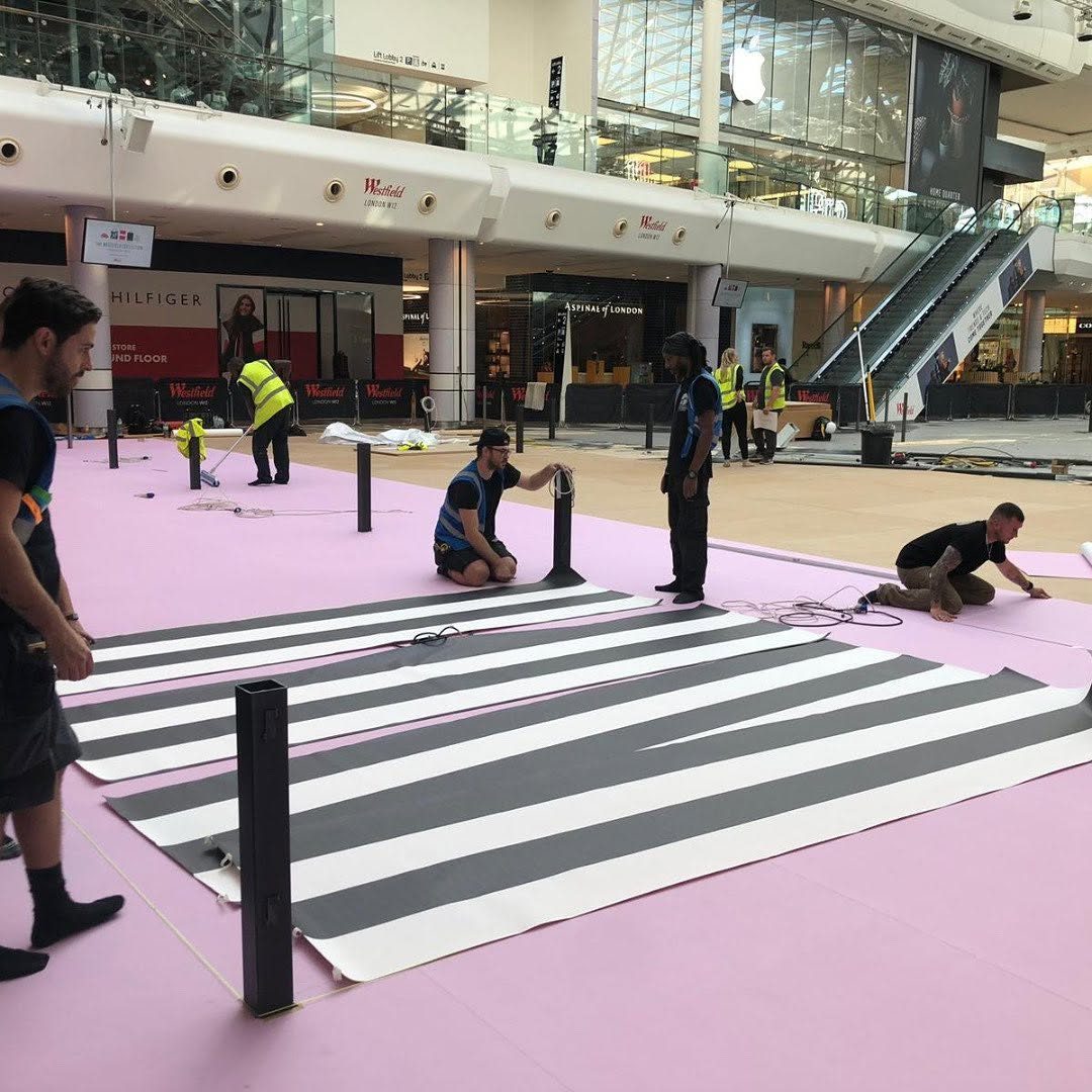 Installers laying black and white striped printed floor vinyls over pink flooring in the atrium at Westfield White City