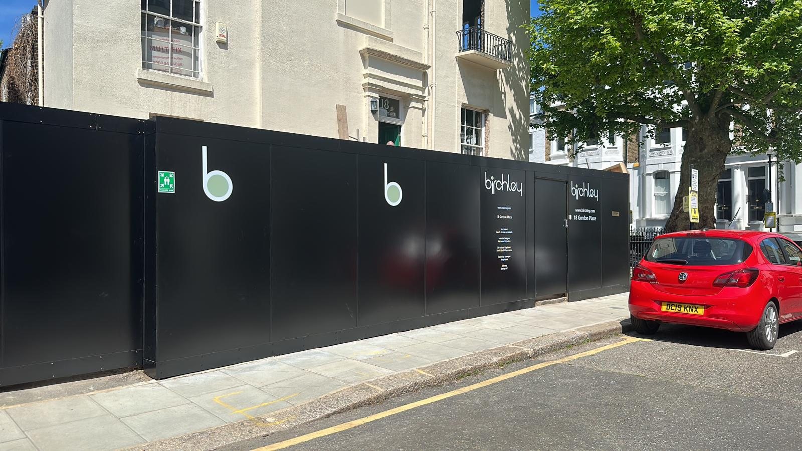 Sleek black site hoarding for Birchley at 18 Gordon Place, London, with a minimal logo, project team credits and a matching door