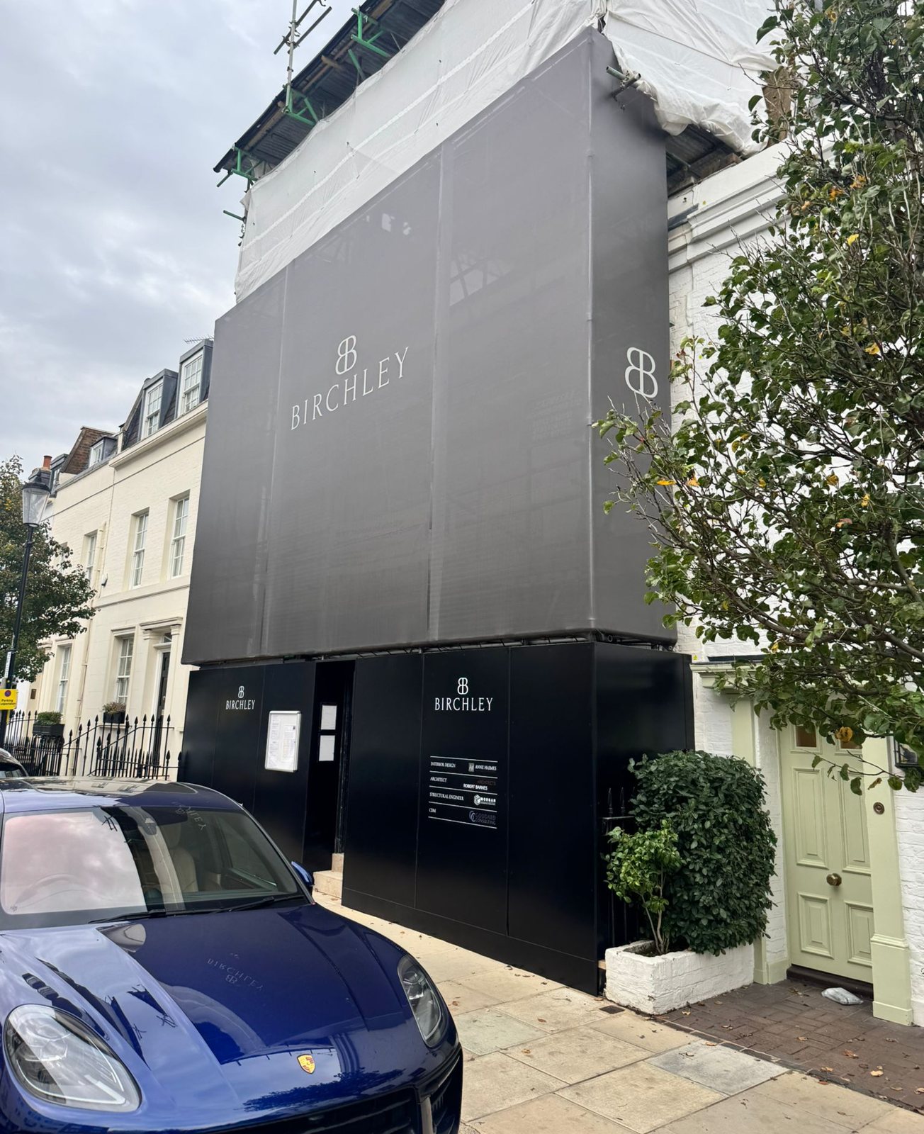 Black Birchley hoarding at street level with a matching grey branded scaffold wrap above on a white London townhouse
