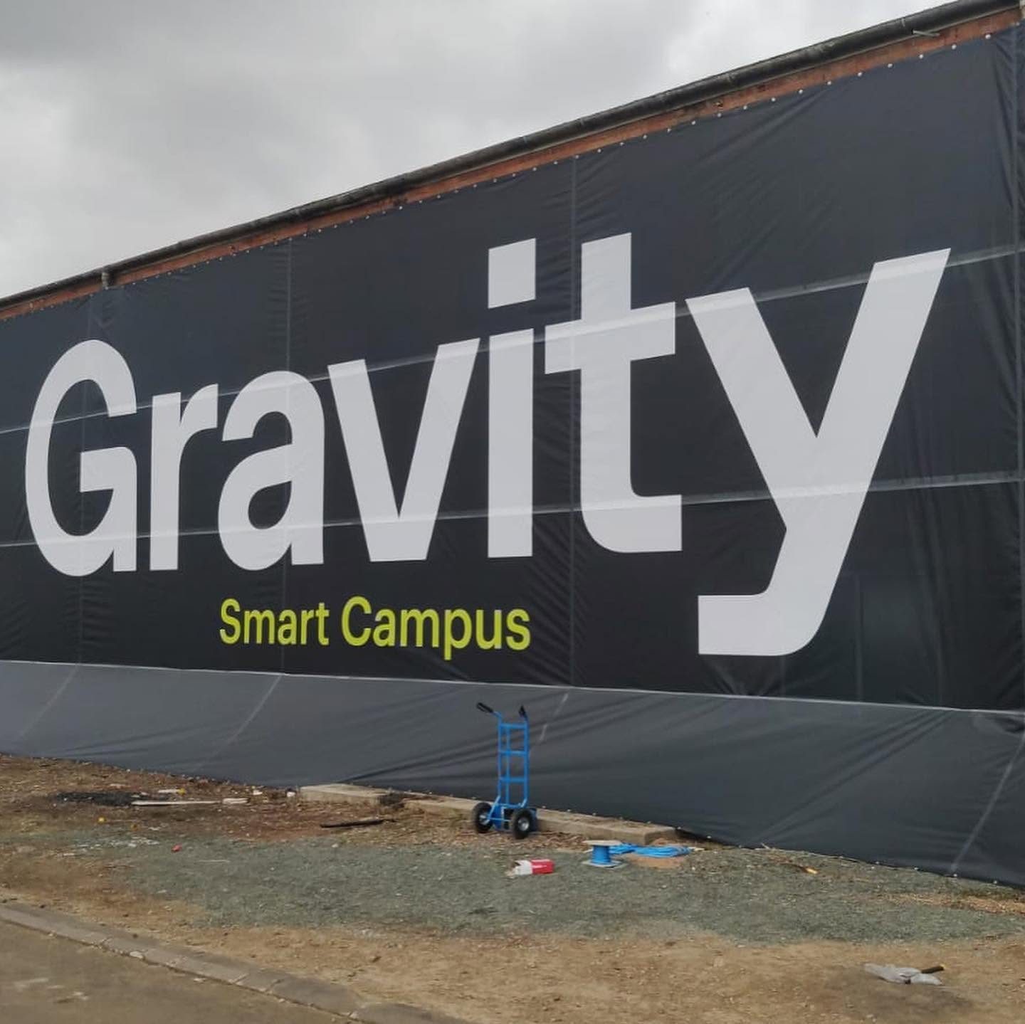 Giant black Gravity Smart Campus building wrap in white and lime lettering stretched across the full length of a brick warehouse