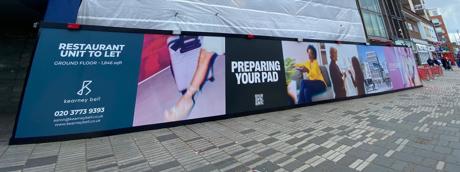 Long printed construction hoarding for YOTELPAD Stratford with lifestyle photography, a restaurant unit to let panel and a QR code
