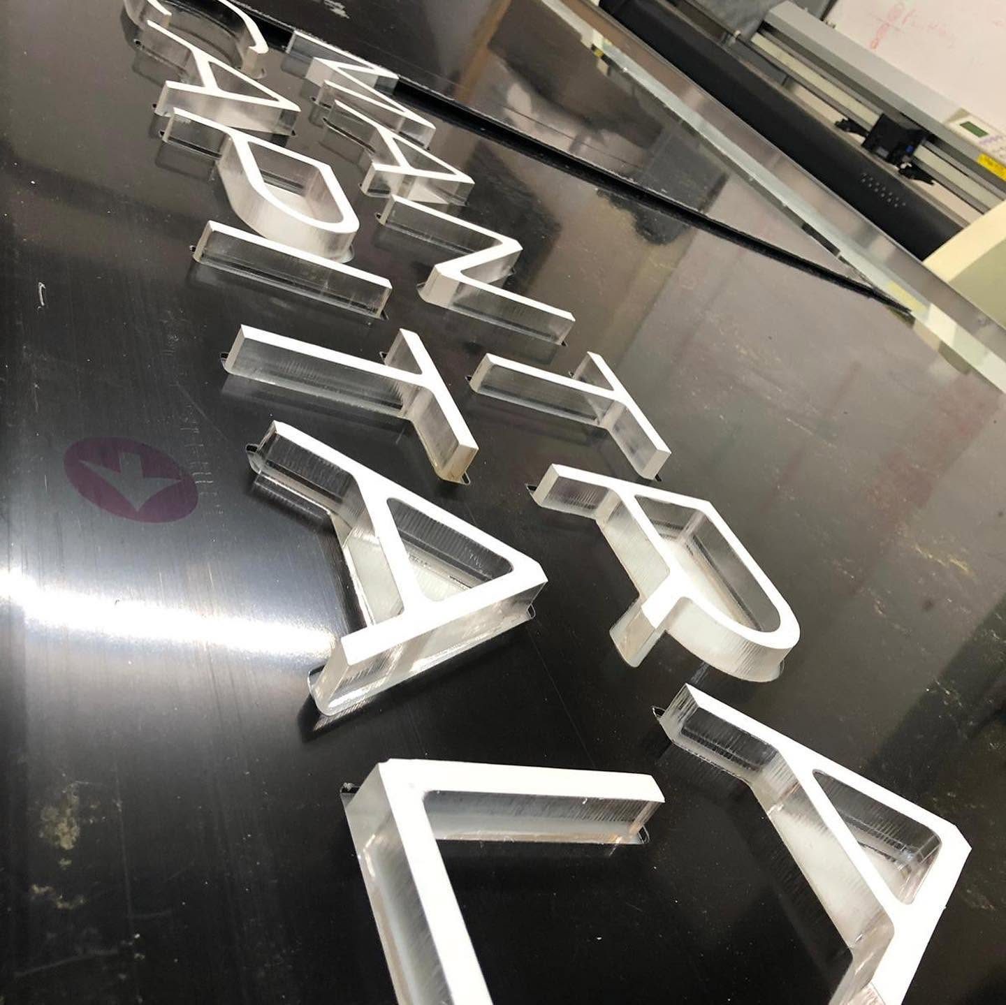 Thick clear acrylic letters freshly cut on the Zund, lying on a black sheet in the workshop