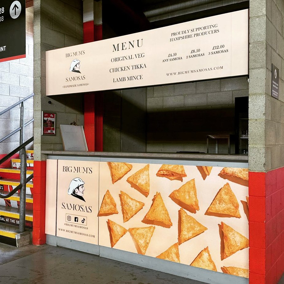 Big Mum's Samosas food stall with a printed menu board above the hatch and a counter front covered in golden samosas