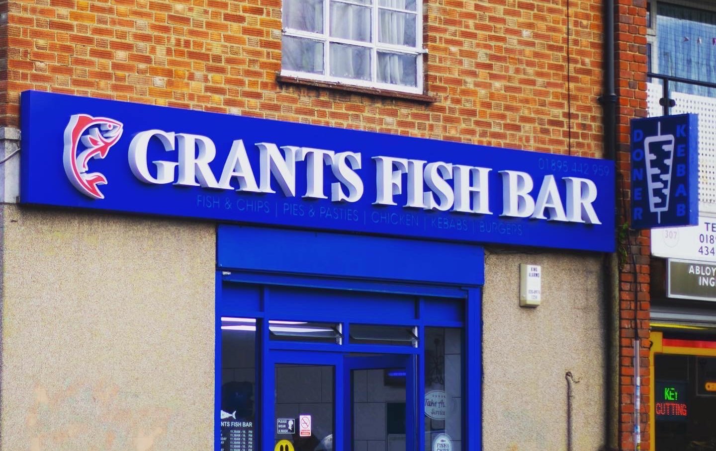 Blue Grants Fish Bar shop fascia with raised white 3D letters, a red fish logo and a projecting doner kebab sign