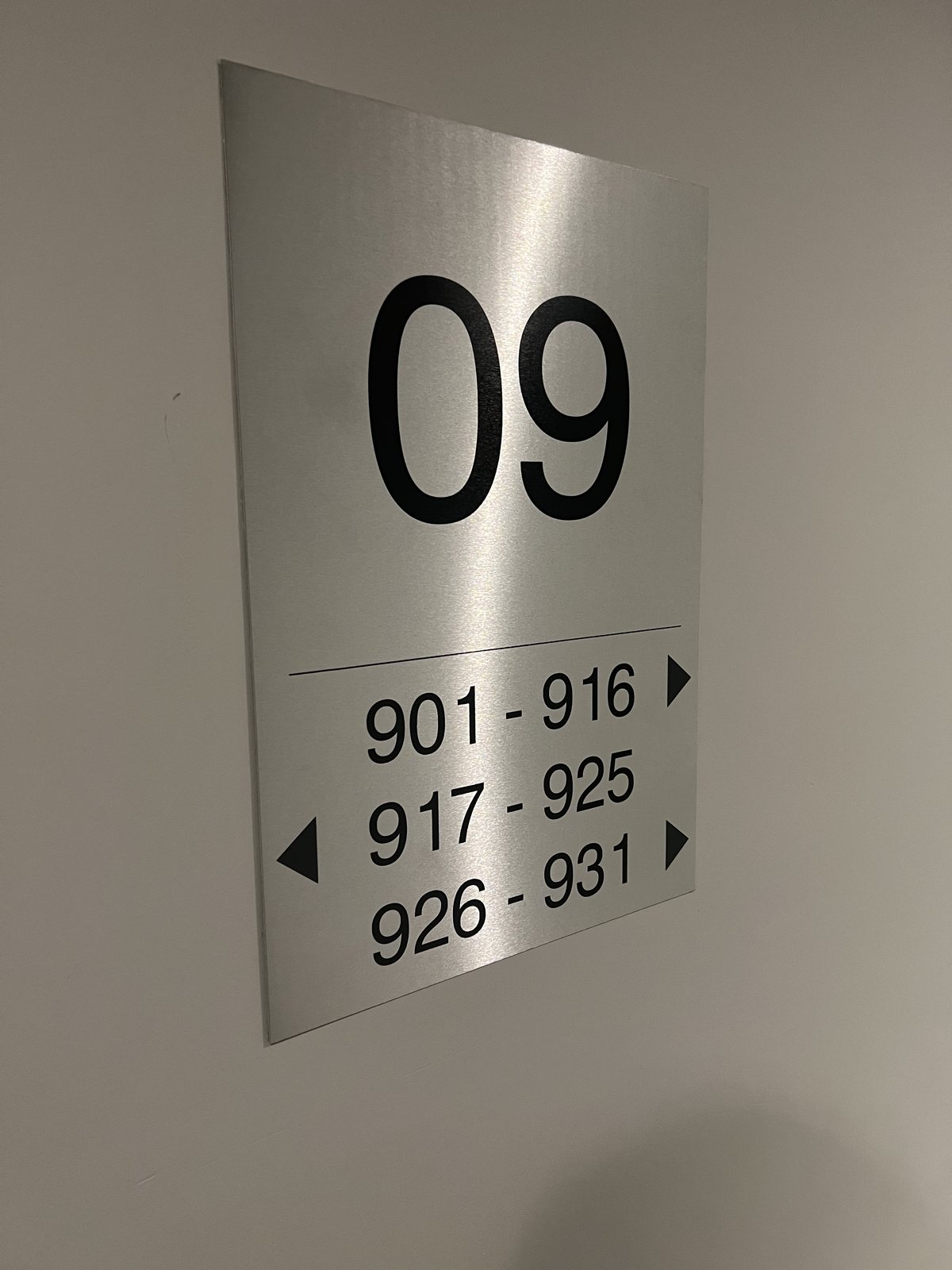 Brushed silver Dibond hotel wayfinding sign for floor 09 with room number ranges and direction arrows printed in black