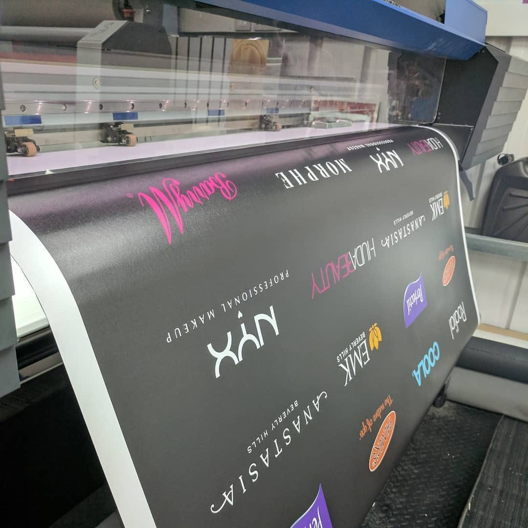 Black wall vinyl printed with beauty brand logos in white, pink and colour coming off a wide format printer in the workshop
