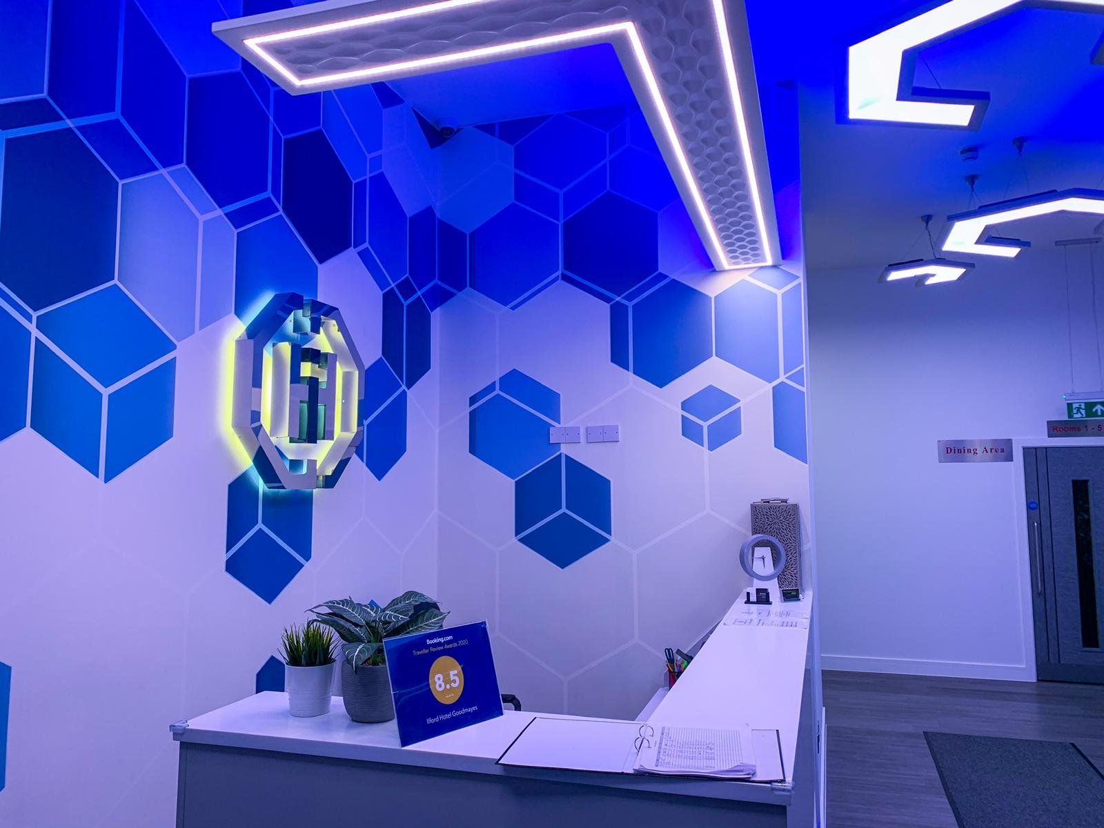 Blue hexagon branded wallpaper behind the reception desk at Ilford Hotels with an illuminated logo