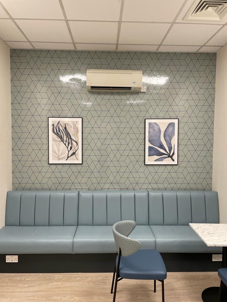 Sage green geometric anti bacterial wallpaper behind blue banquette seating in an NHS staff breakout room