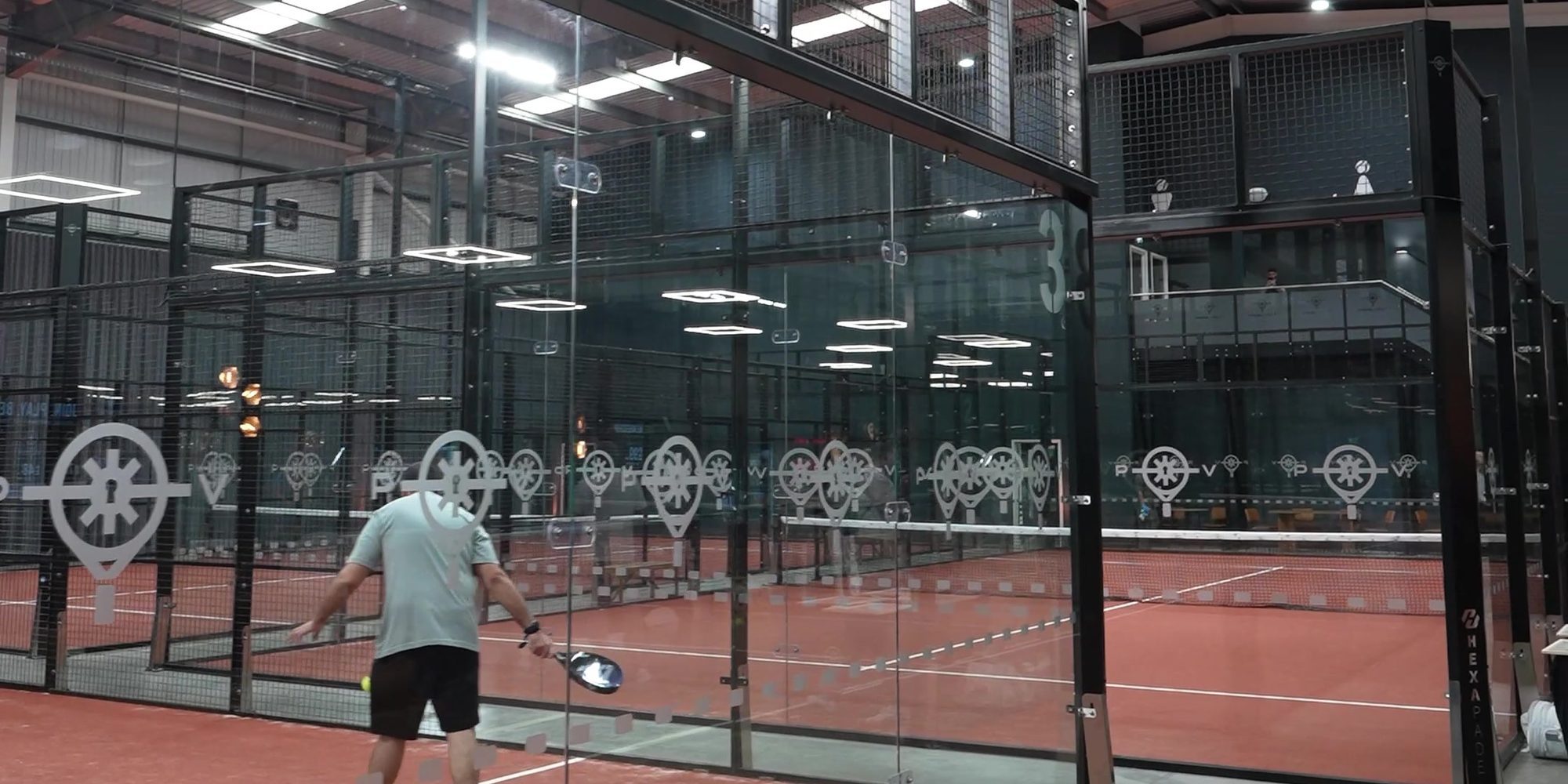 Padel Vault frosted logo decals across the glass of the indoor courts
