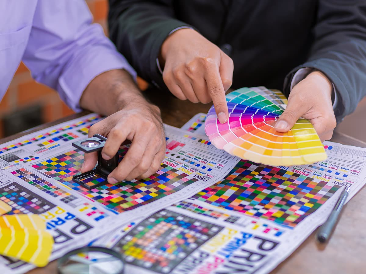 Checking CMYK test prints with a loupe and colour swatches