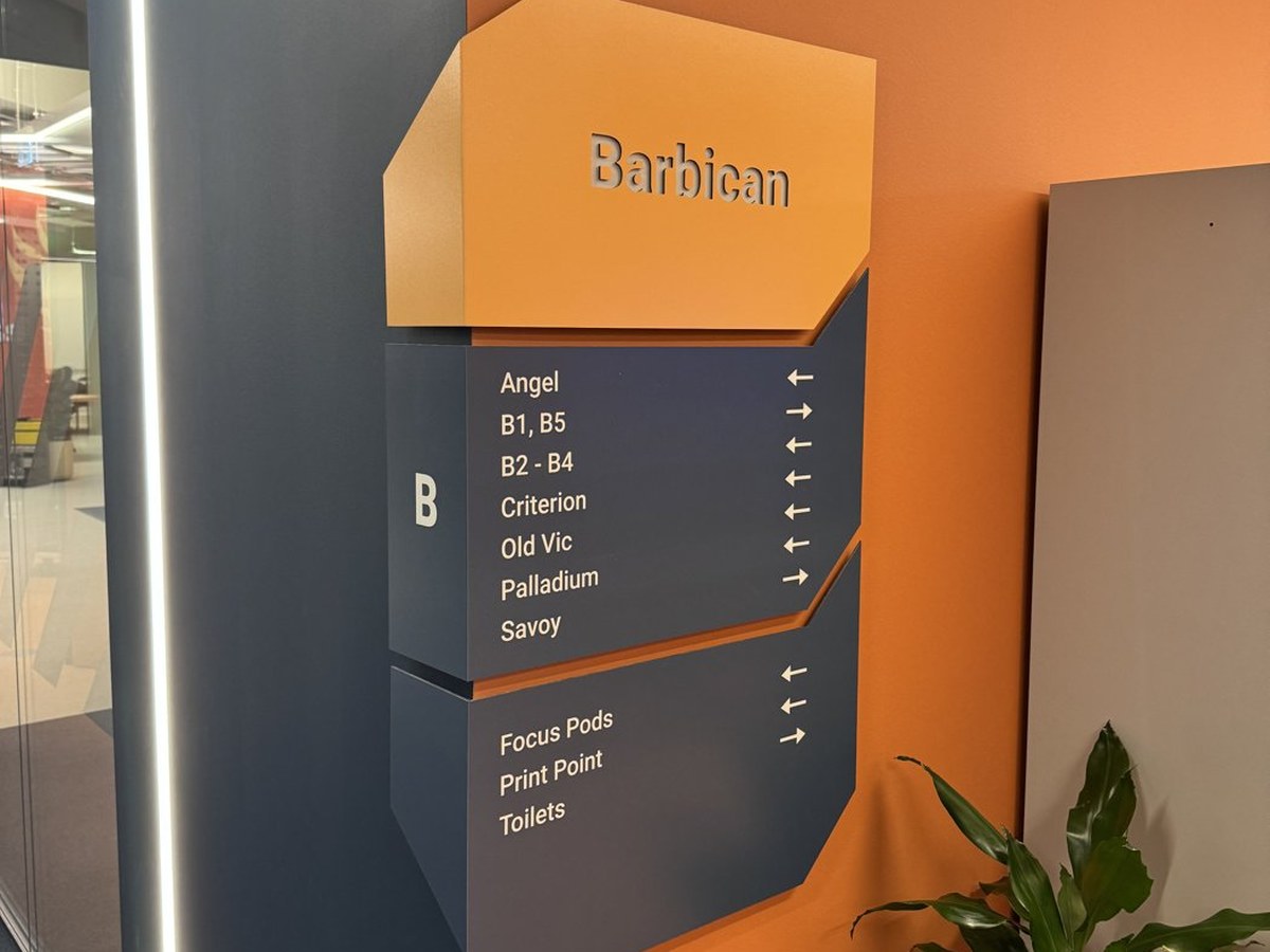 Printed Barbican way finding sign with room directions on an orange office wall