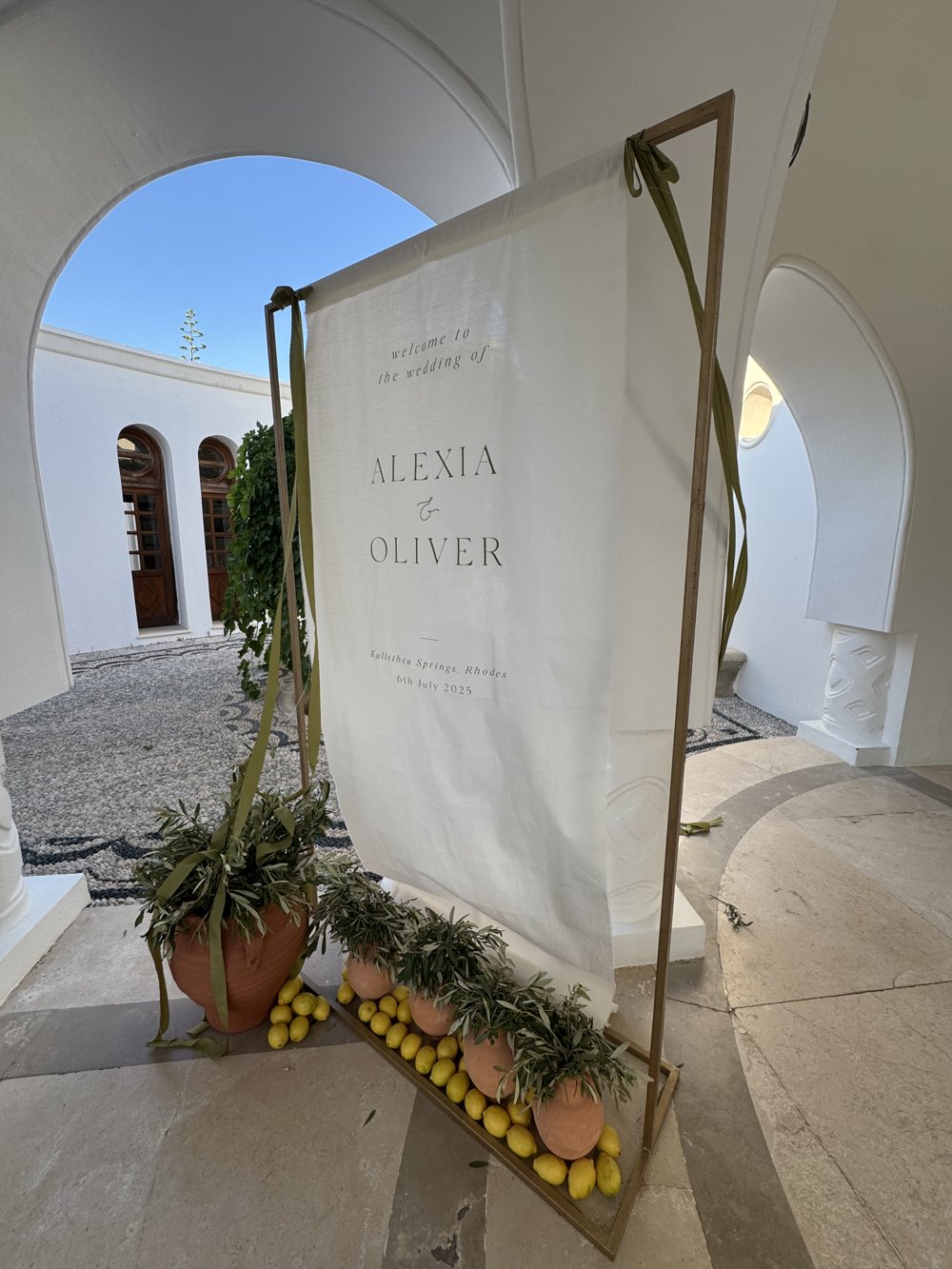 Fabric wedding welcome sign on a gold frame with olive trees and lemons